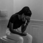 Black and white image of a young woman holding a pregnancy test, displaying anxiety.