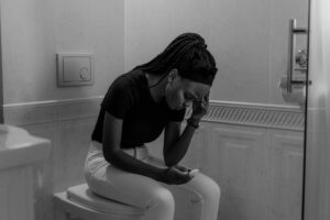 Black and white image of a young woman holding a pregnancy test, displaying anxiety.