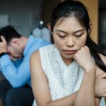 A couple experiencing relationship tension sitting silently on a sofa.