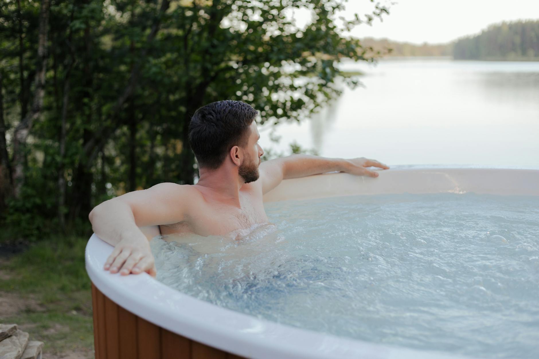 A man enjoys a serene moment in a jacuzzi overlooking a peaceful lake.