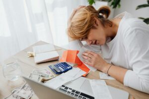 A woman overwhelmed with finances, surrounded by bills, calculator, and cash at home.