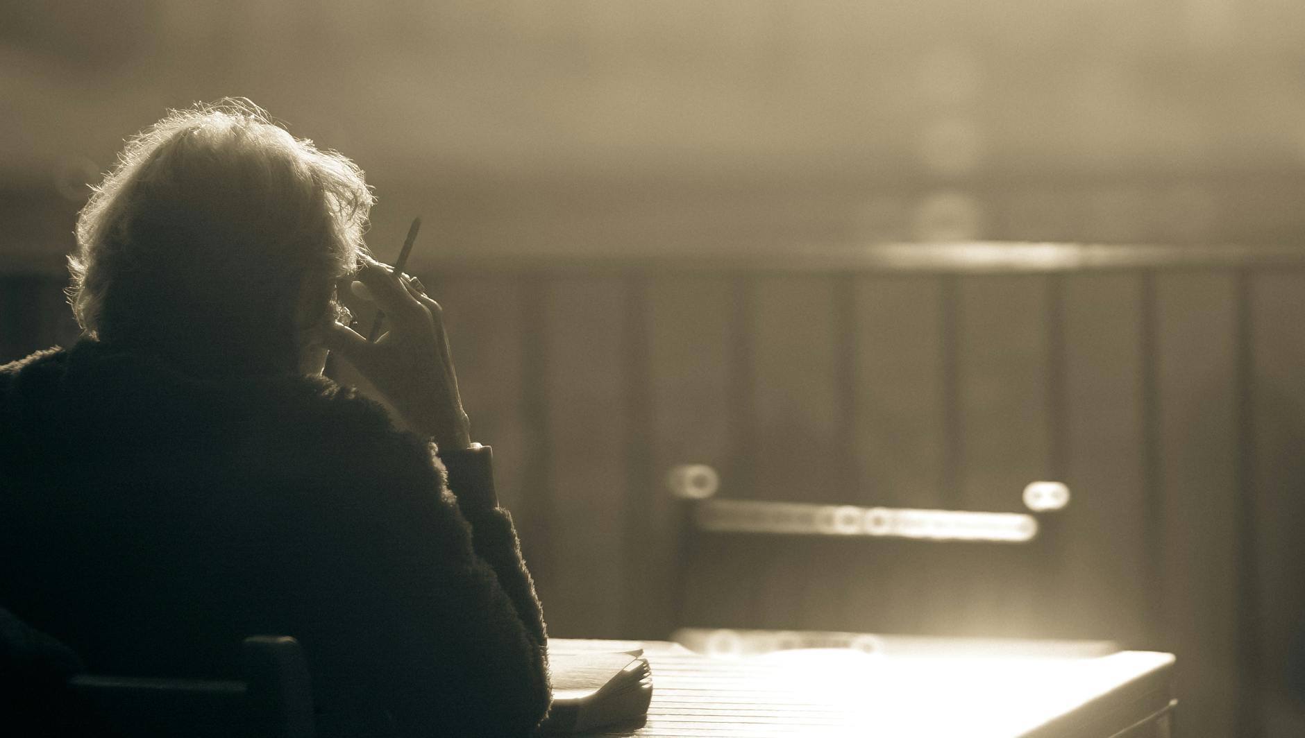 Serene sepia photo capturing an elderly woman enjoying a peaceful outdoor moment with a cigarette.