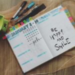 Open planner with handwritten notes and colorful pens on a wooden table promoting positivity.