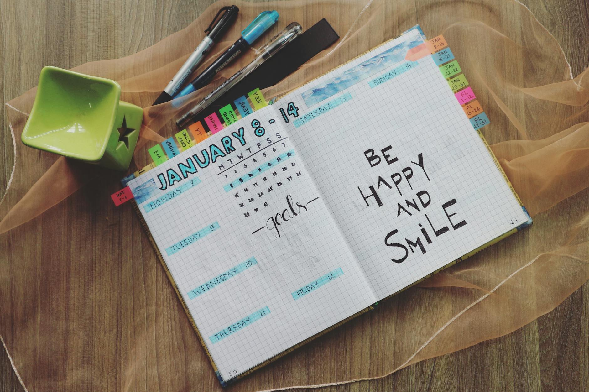 Open planner with handwritten notes and colorful pens on a wooden table promoting positivity.