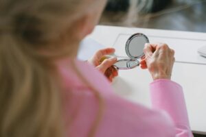 Elderly woman in pink holding a pocket mirror, focused close-up image.
