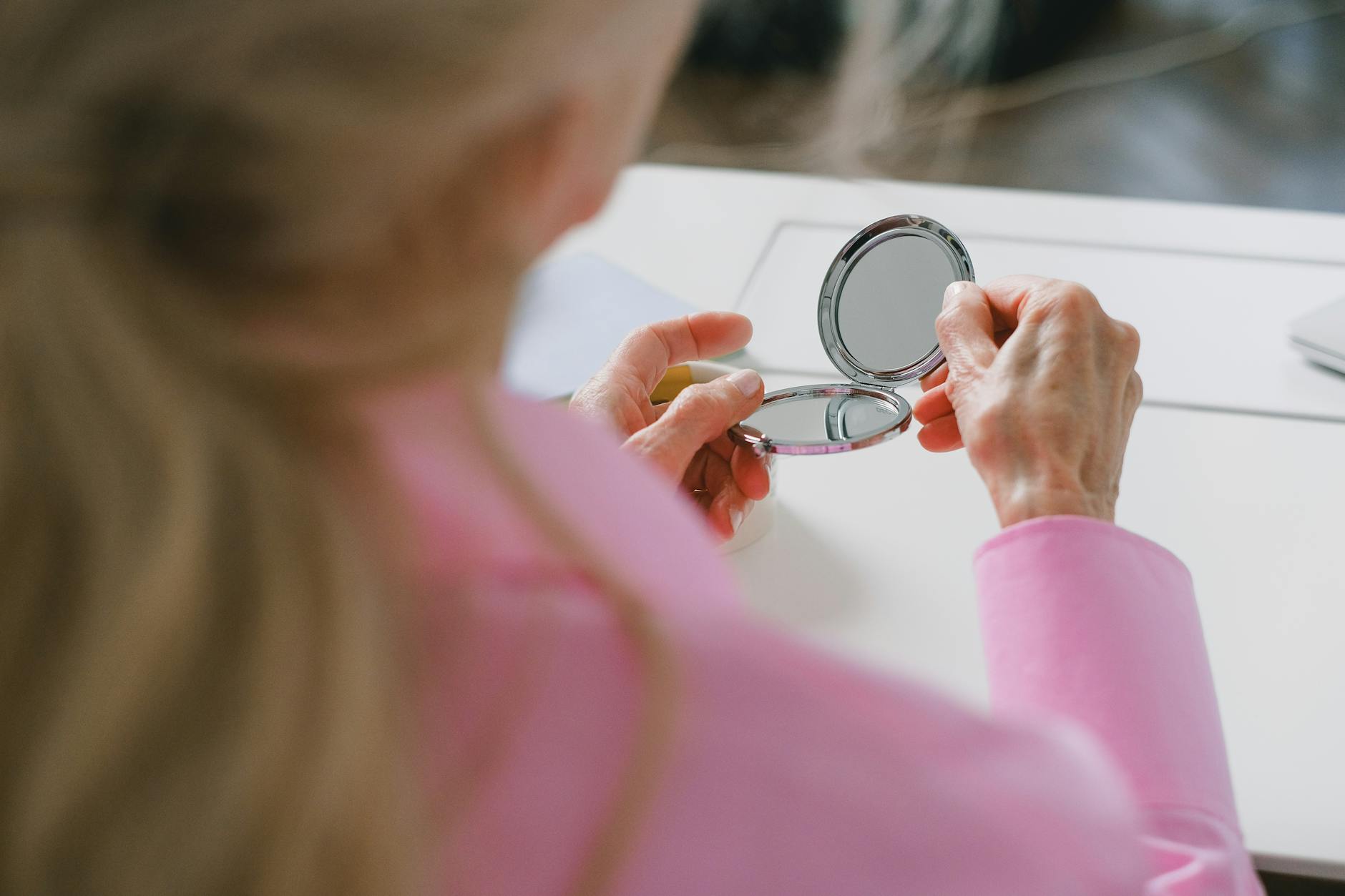Elderly woman in pink holding a pocket mirror, focused close-up image.