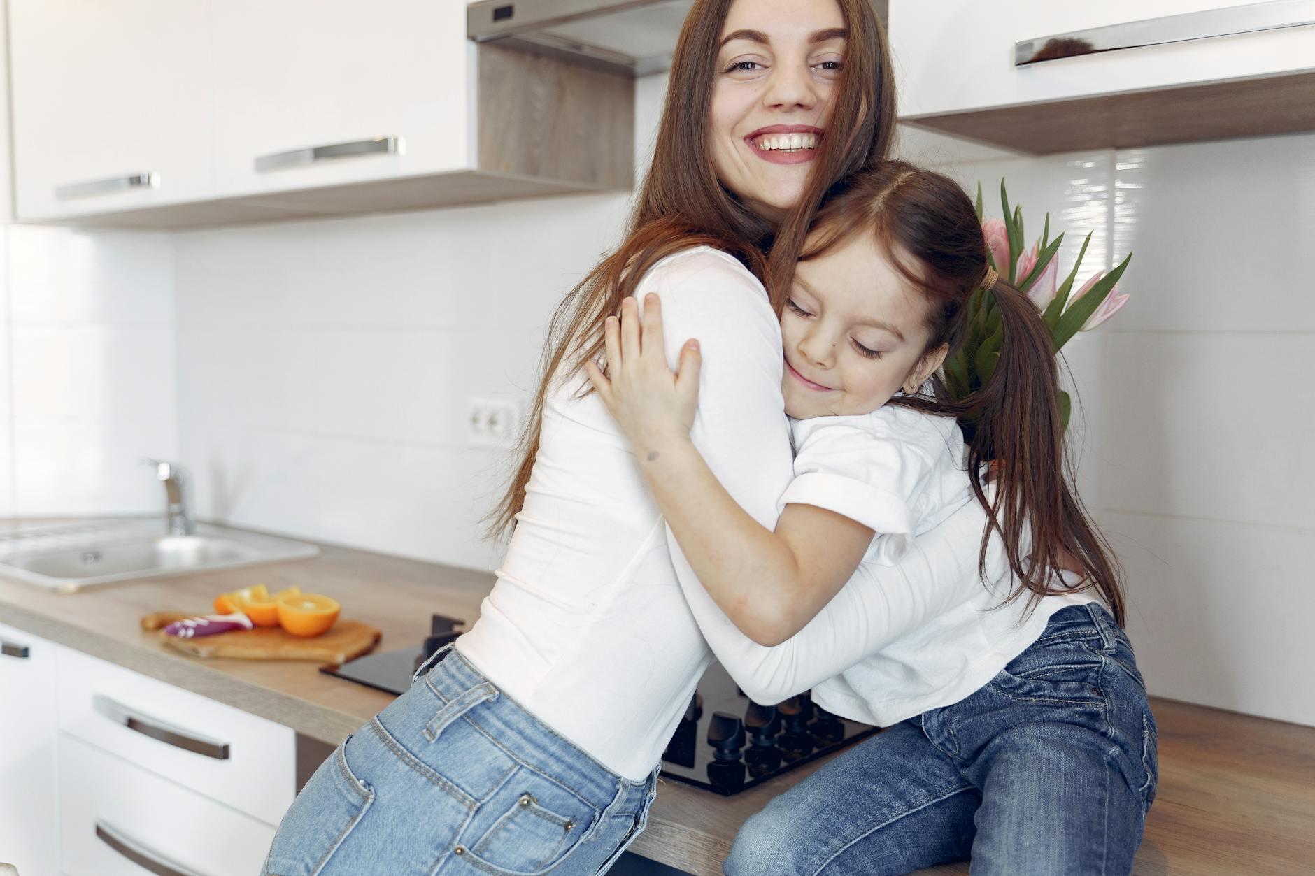 A joyful moment of a mother and daughter hugging in a modern kitchen setting.
