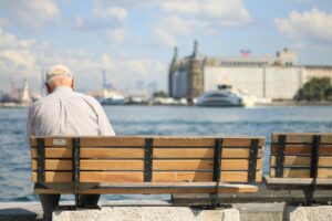 An elderly man sits alone on a bench by the waterfront, enjoying a peaceful day.