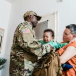 A soldier in uniform comforts his child at home with his partner.