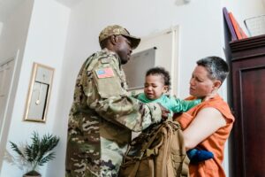 A soldier in uniform comforts his child at home with his partner.