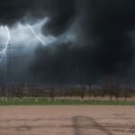 Intense lightning strikes during a storm over a countryside landscape with power lines.