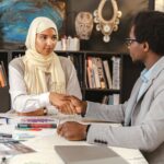 African American man and Arabic woman shaking hands at a desk in a modern office.