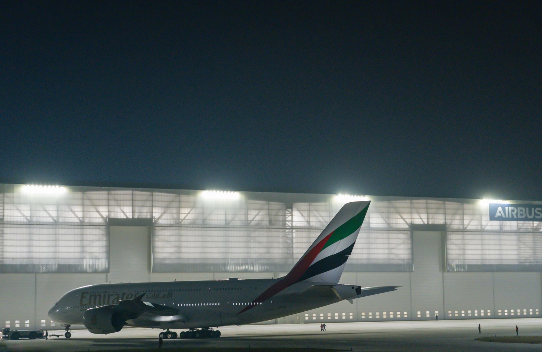 A serene scene of an Emirates Airbus A380 aircraft stationed at an airport hangar illuminated at night.