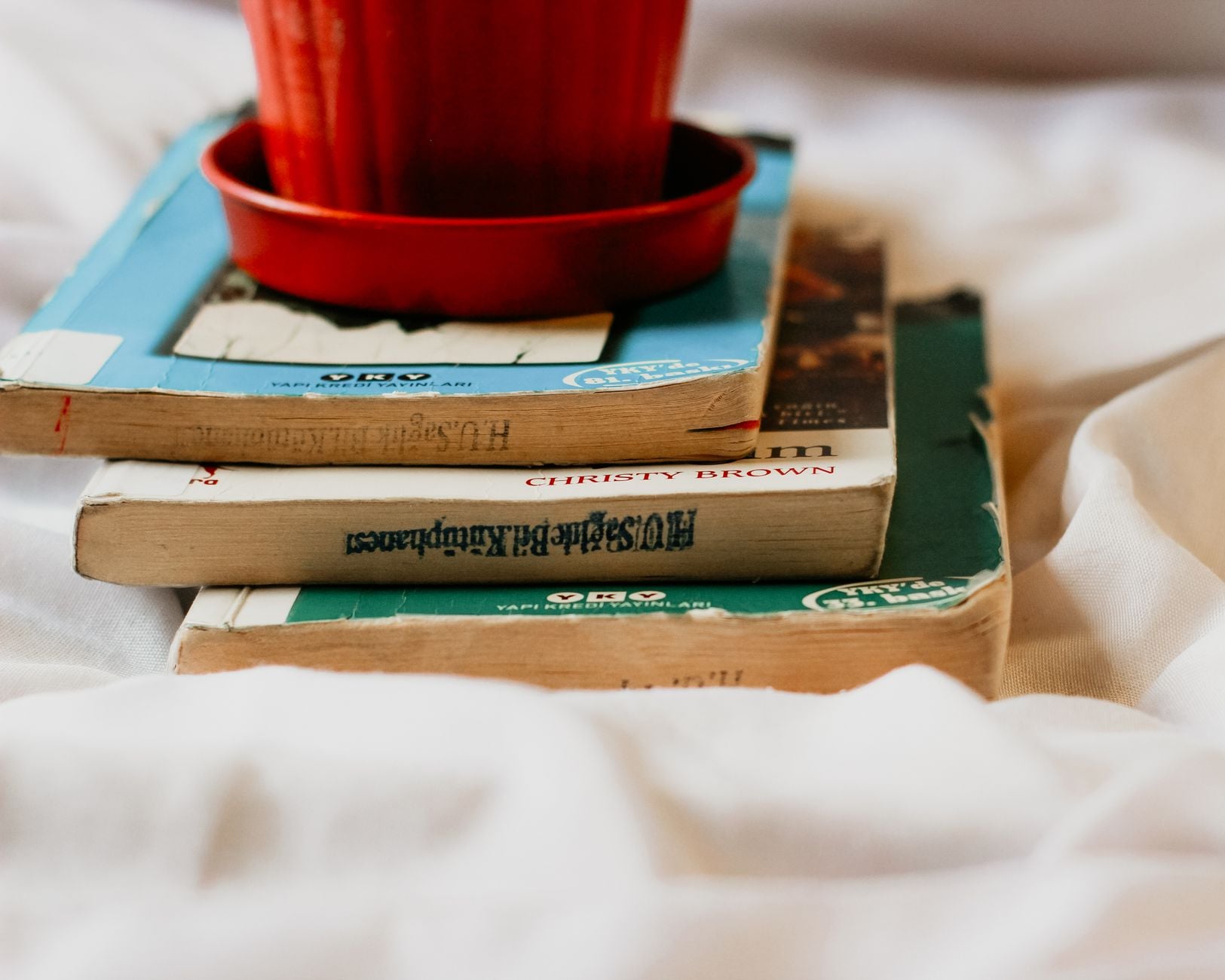 A stack of vintage books topped with a red pot, perfect for themes of literature and learning.