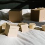 Cardboard boxes with lids arranged on a sunlit bed, casting shadows.