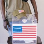 Adult voter standing by a ballot box with American flag, symbolizing democracy and election participation.