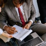 A businessman in a suit signing a contract with colleagues' assistance.