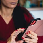 Close-up of a woman using a smartphone indoors, focusing on hands with red nails.