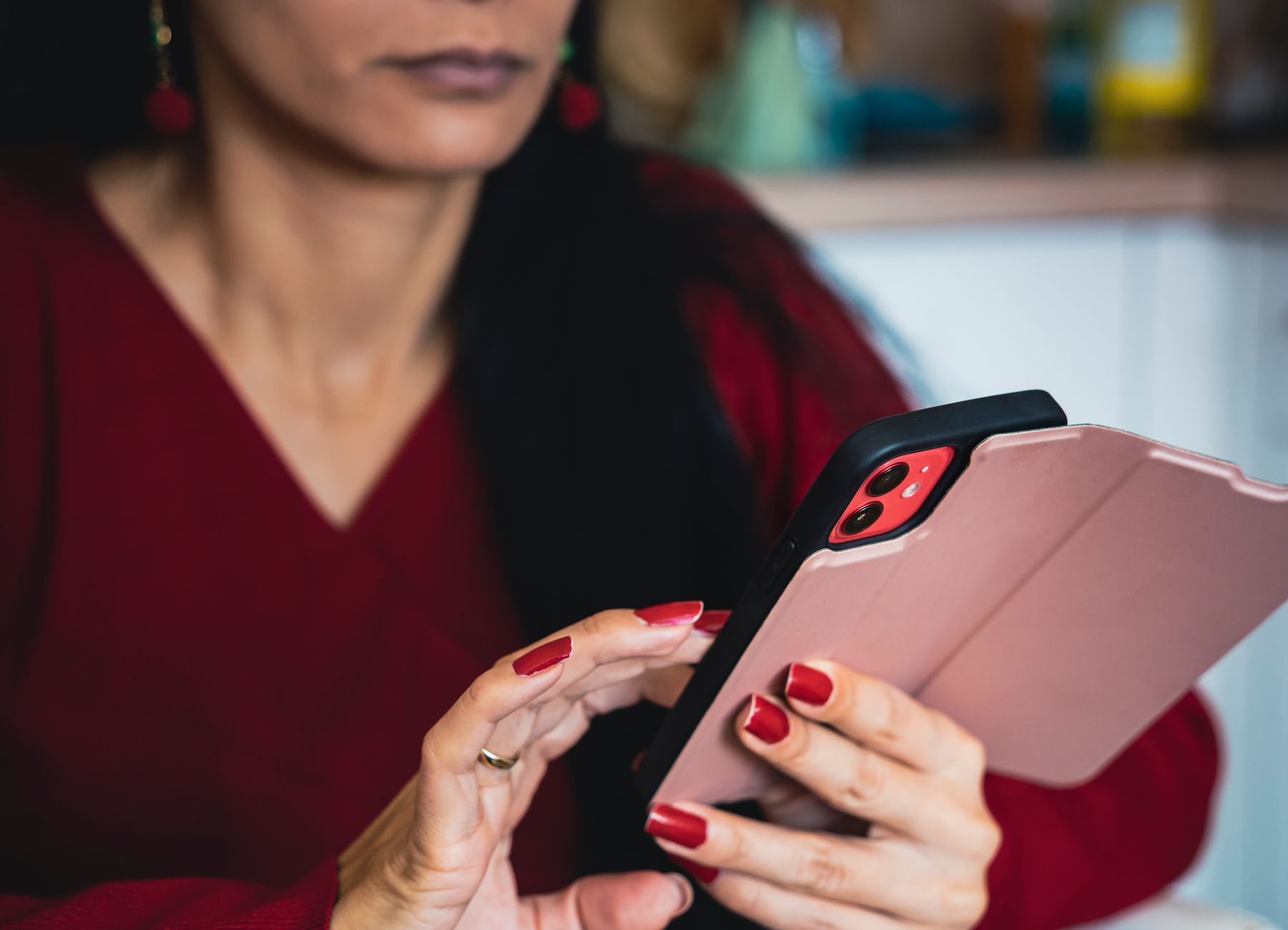 Close-up of a woman using a smartphone indoors, focusing on hands with red nails.