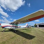 A light aircraft parked on a clear day near a hangar at an airport, showcasing aviation design.