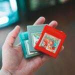 Hand holding vintage Pokemon game cartridges, showcasing nostalgic gaming.