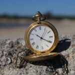 Close-up of an old-fashioned pocket watch resting on a rock at a beach.