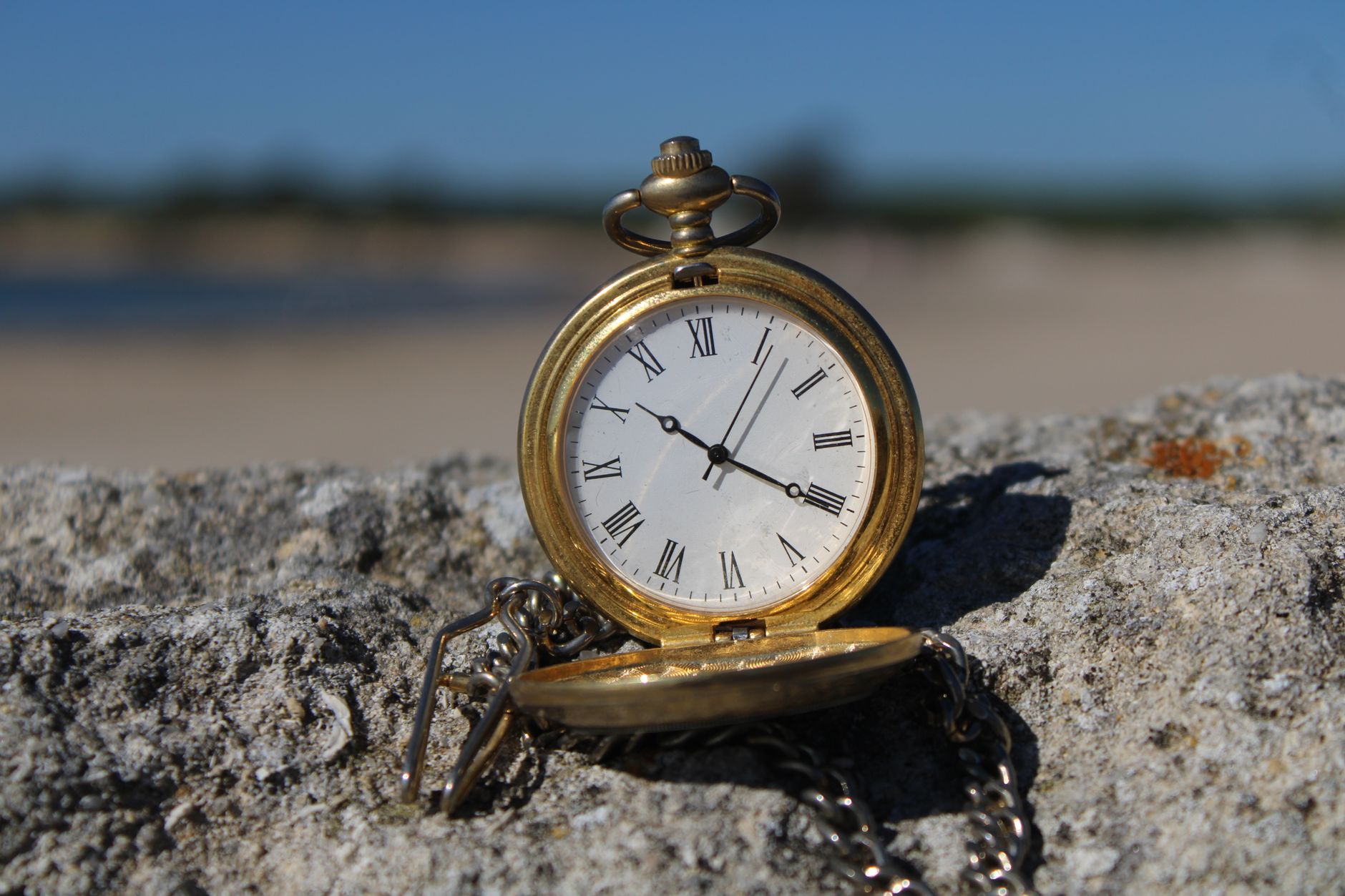 Close-up of an old-fashioned pocket watch resting on a rock at a beach.