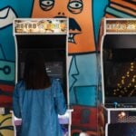 Woman engages in retro arcade gaming in a vibrant, graffiti-themed environment.