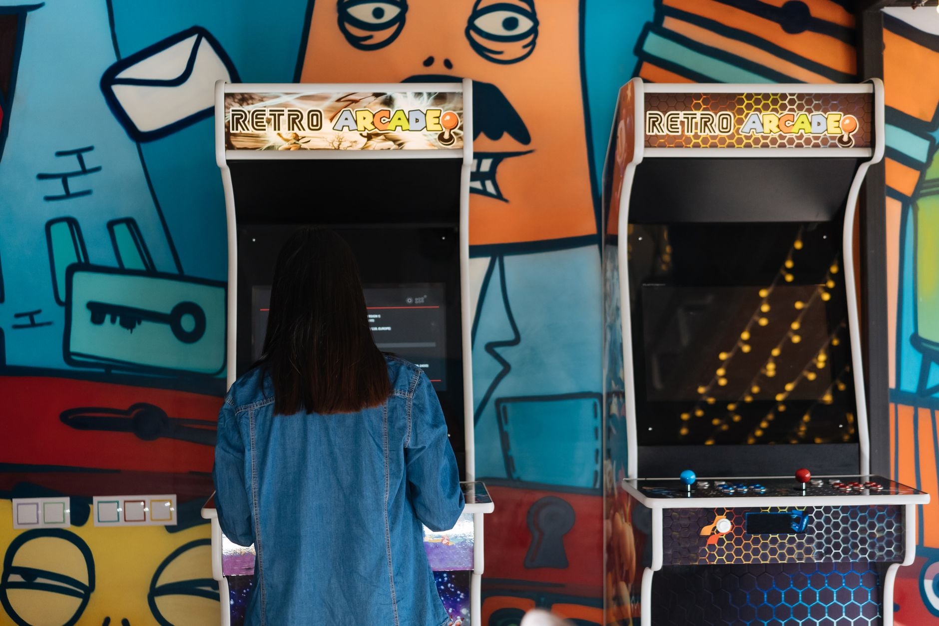 Woman engages in retro arcade gaming in a vibrant, graffiti-themed environment.
