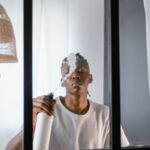 A young man uses a spray bottle to clean a glass window inside a modern room.